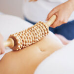 A wood therapy tool being pressed onto someones stomach.